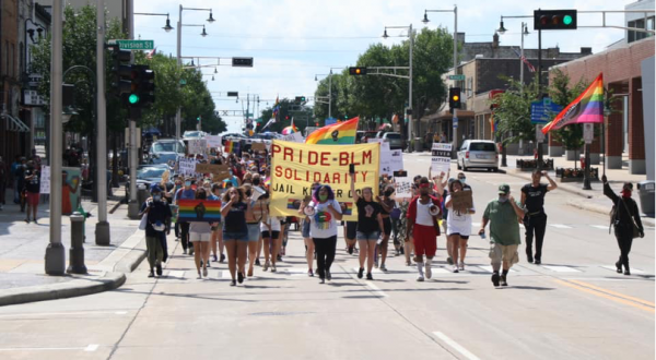 Protestors marching down the middle of the street holding Pride flags and a banner that reads "Pride-BLM Solidarity"