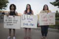 Three young women hold up signs reading "there is no such thing as somone else's children," "we belong to each other," and "get close enought to love them."