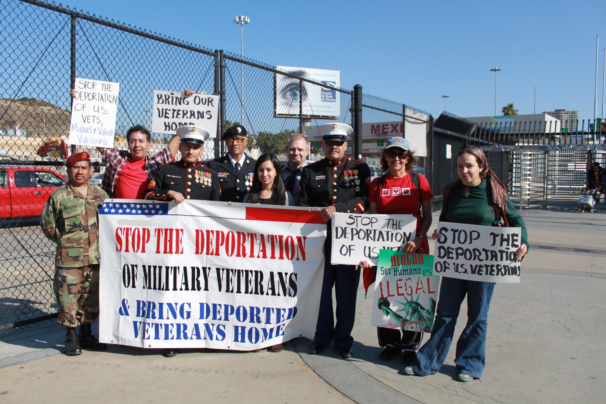 Military veterans in uniform with their families holding sign reading "stop the deportation of military veterans" at border port of entry