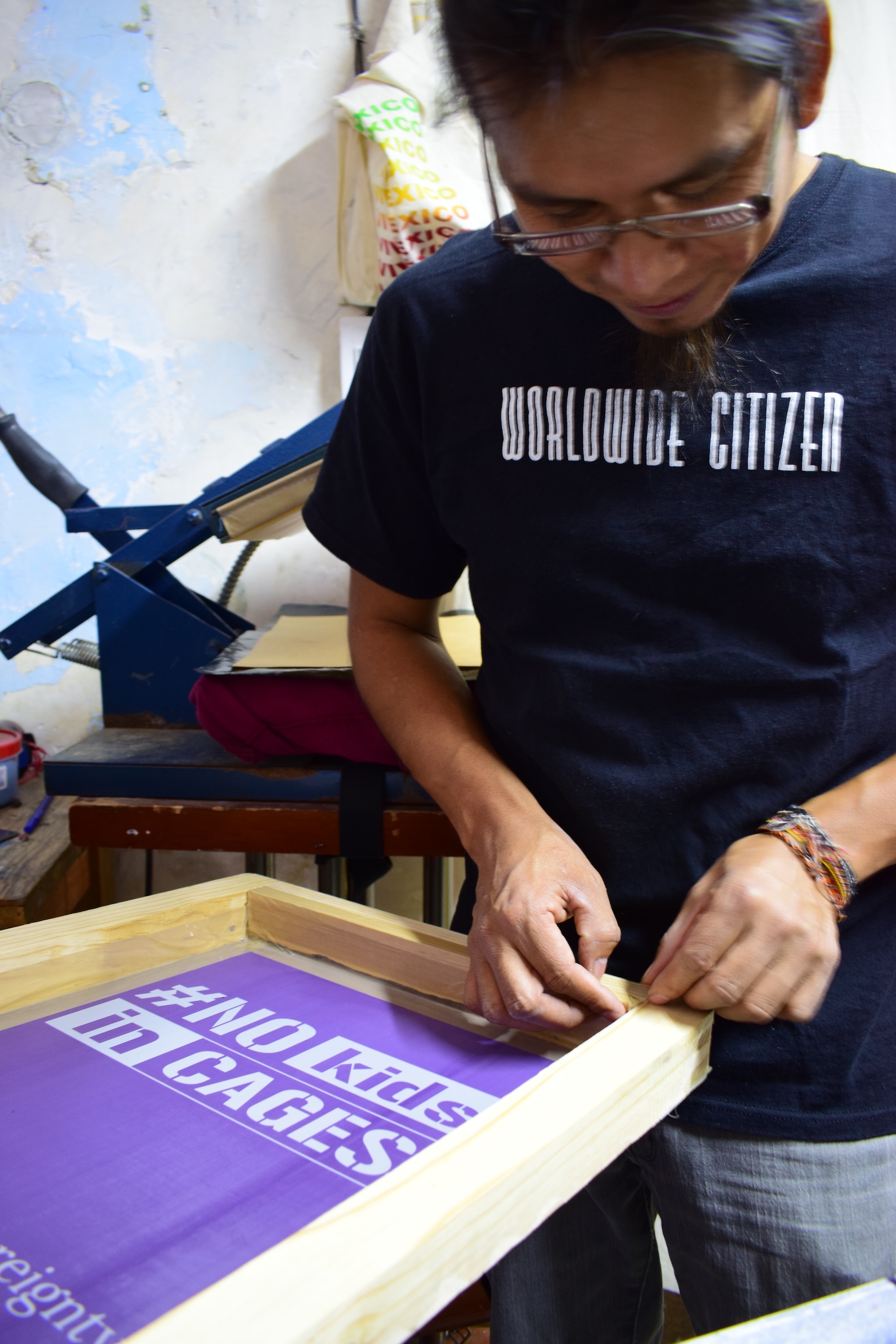 Diego at his printing shop preparing a screen print and wearing t-shirt that reads "worldwide citizen"