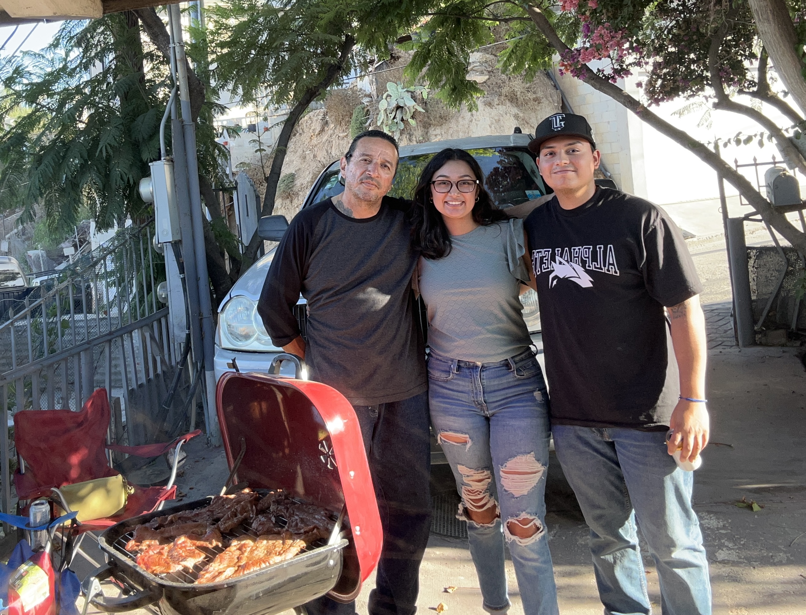 Author with uncle and partner grilling meet outdoors in Tijuana yard.