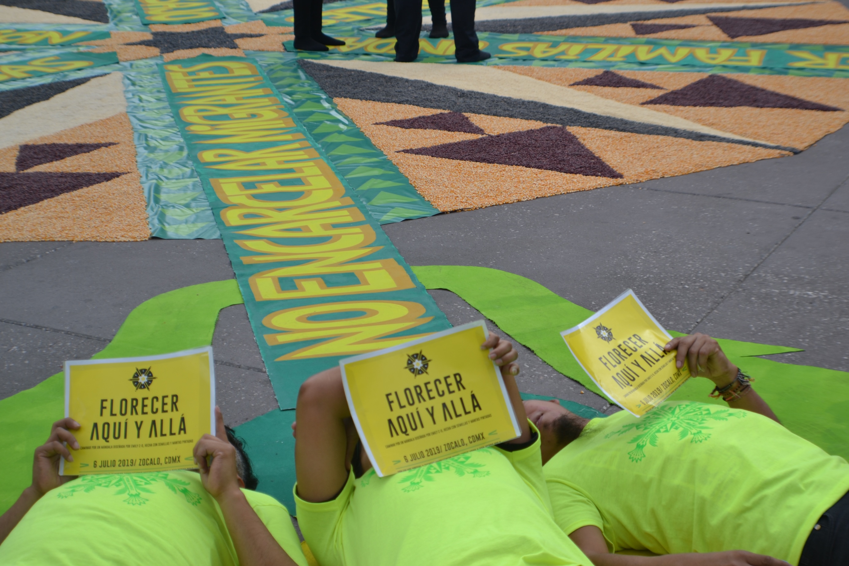 Three people laying down and holding up signs for the "Florecer Aqua Y Allá" event.