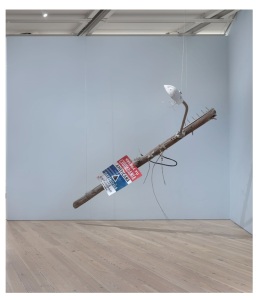 lamppost handing from ceiling on angle with nails protruding and a red, white and blue sign announcing that viewers should value American citizenship