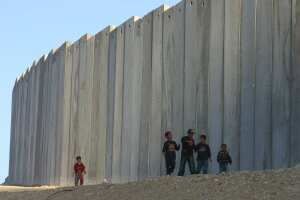 children walking on side of massive border wall in occupied West Bank