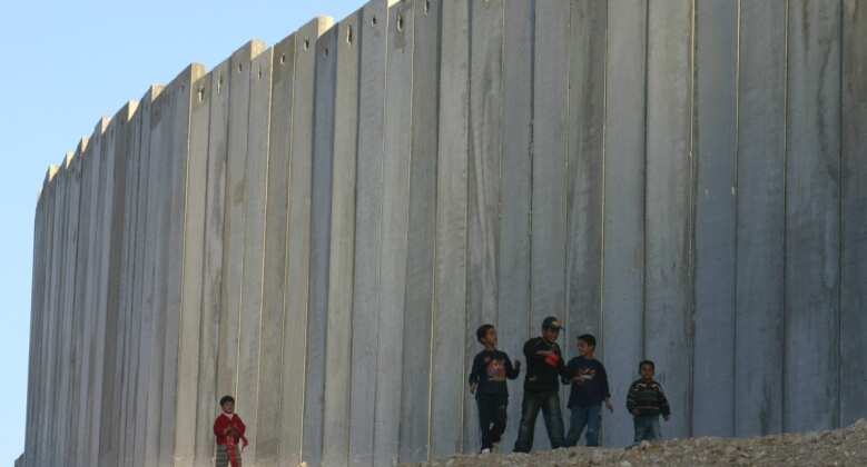 children walking on side of massive border wall in occupied West Bank