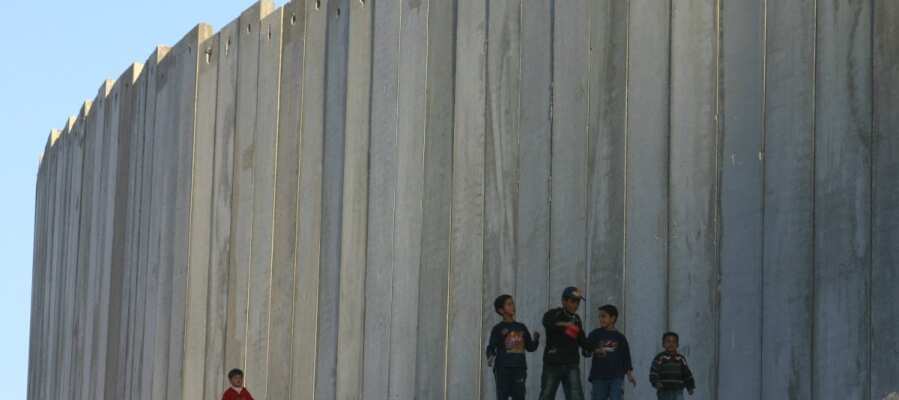 children walking on side of massive border wall in occupied West Bank