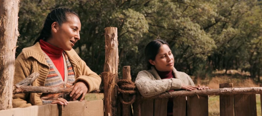 Two women leaning over fence as one woman sings in Quechua.